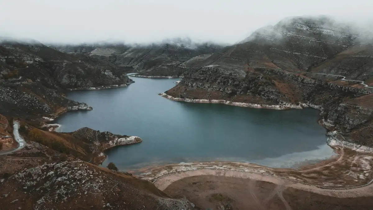 Misty hills rise like wispy brushstrokes around the crystal lake, where ripples dance across the glassy surface, reflecting…