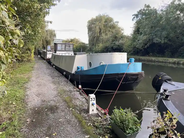 A photo of a canal boat moored at a gravel bank with trees and water visible, overlaid with the text 'i'm not lazy, i'm in…