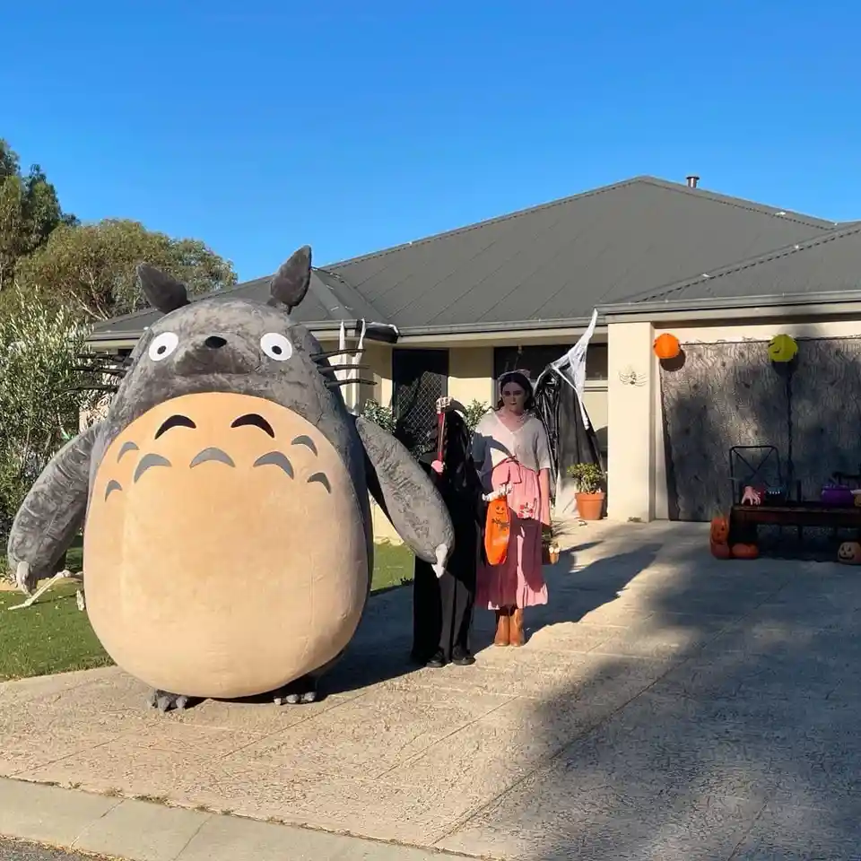 Two people in Halloween costumes stand on a driveway in front of a house decorated for Halloween. One person wears a large…