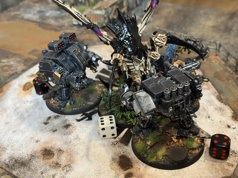 Two heavily armored, intricately painted miniature war machines stand on a textured gaming surface, surrounded by scattered…