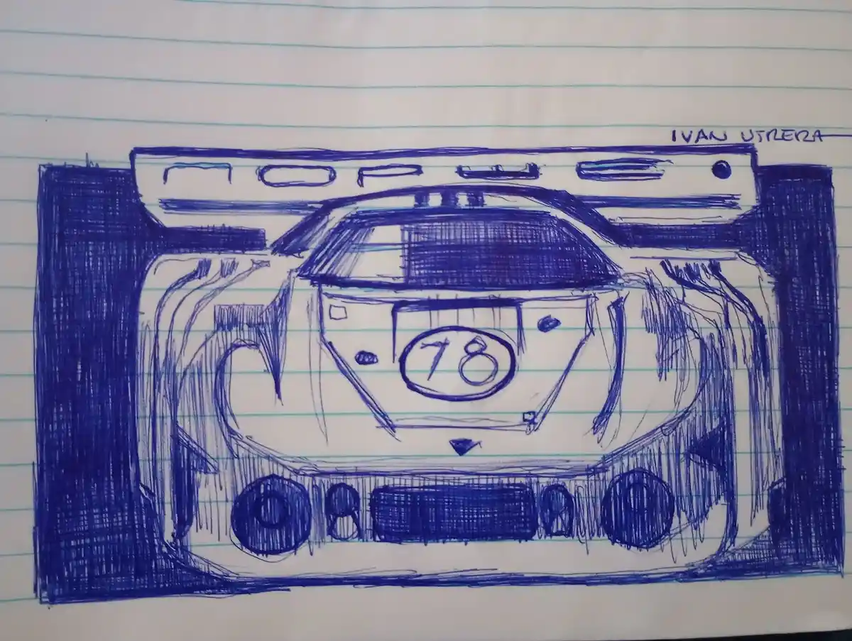 A blue ink drawing on lined notebook paper depicts a stylized race car from the front, featuring a large rear wing, a…