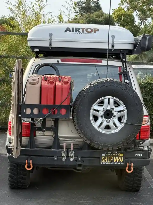 The rear view of a silver SUV heavily modified for off-roading, featuring a roof-top cargo box labeled 'AIRTOP', a spare…