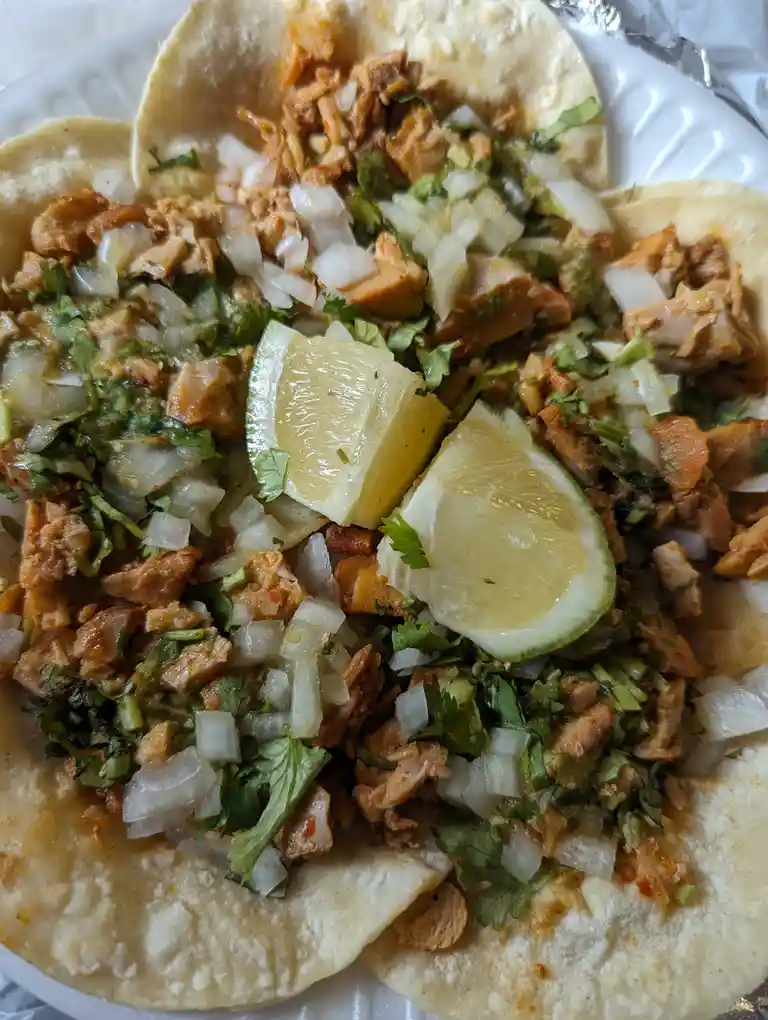 A close-up photo shows several soft corn tortillas filled with shredded meat, chopped white onions, and fresh cilantro…