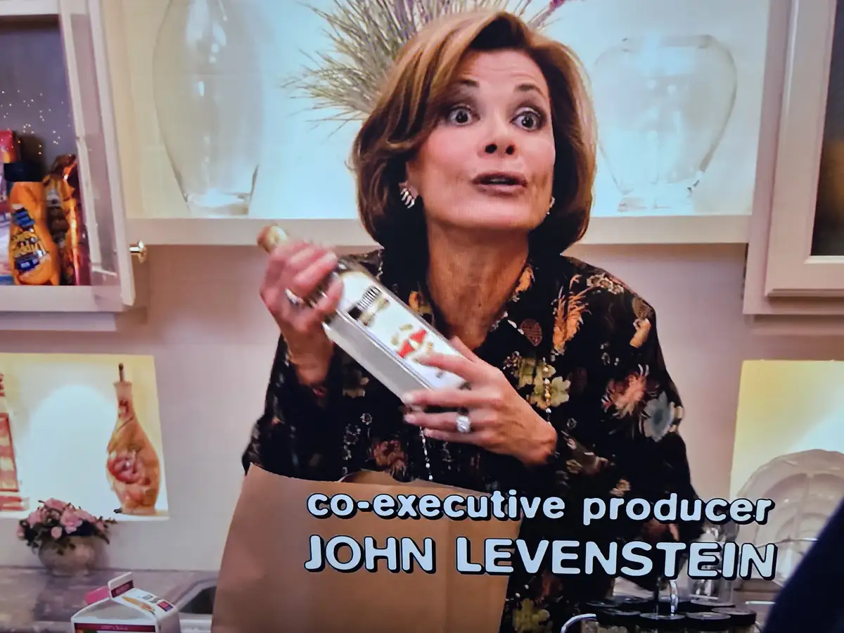 A woman with a surprised expression holds a bottle while standing in a kitchen, with overlaid text reading 'co-executive…