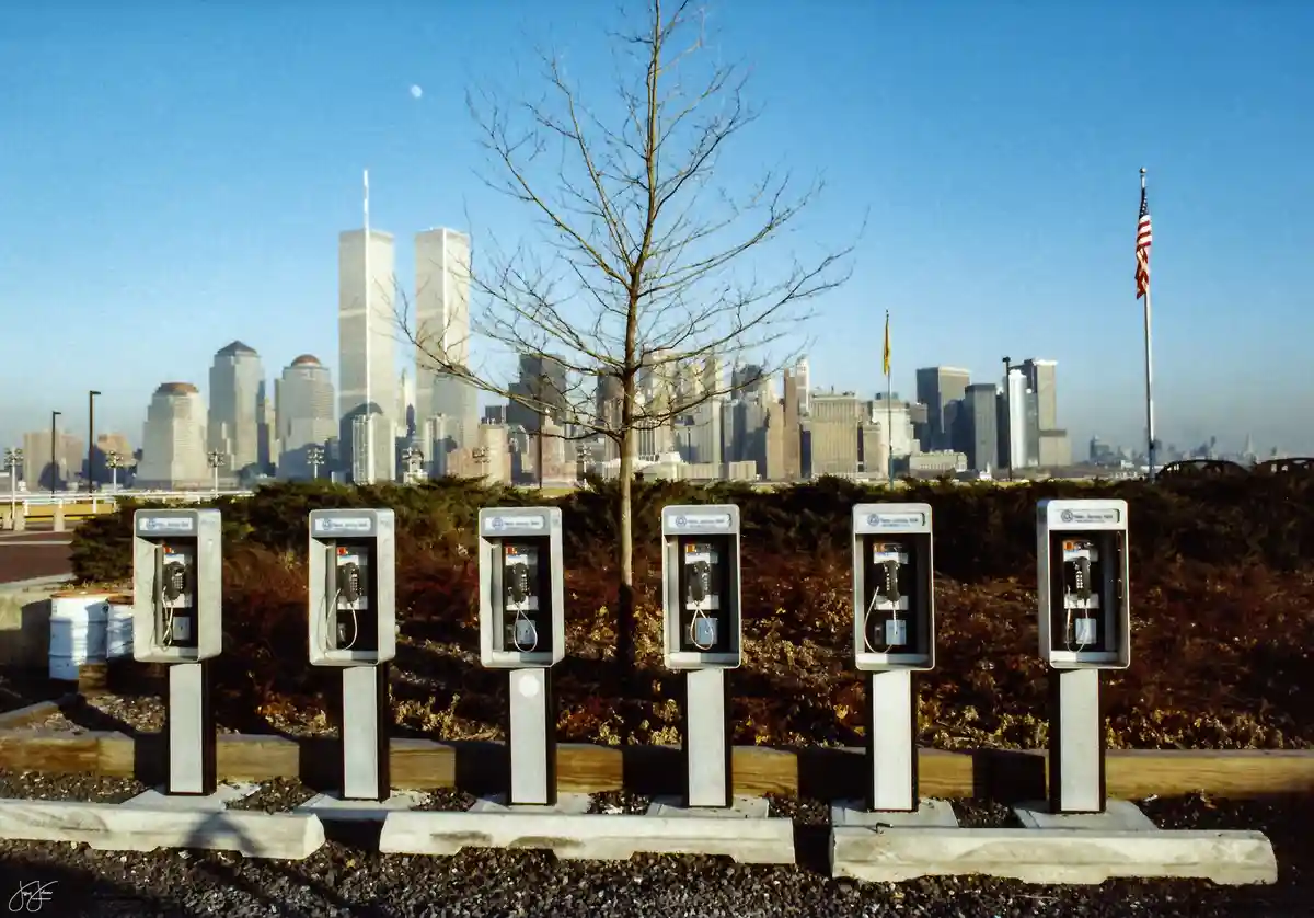 A row of six vintage New Jersey Bell payphones stands in the foreground, with the Twin Towers of the World Trade Center…