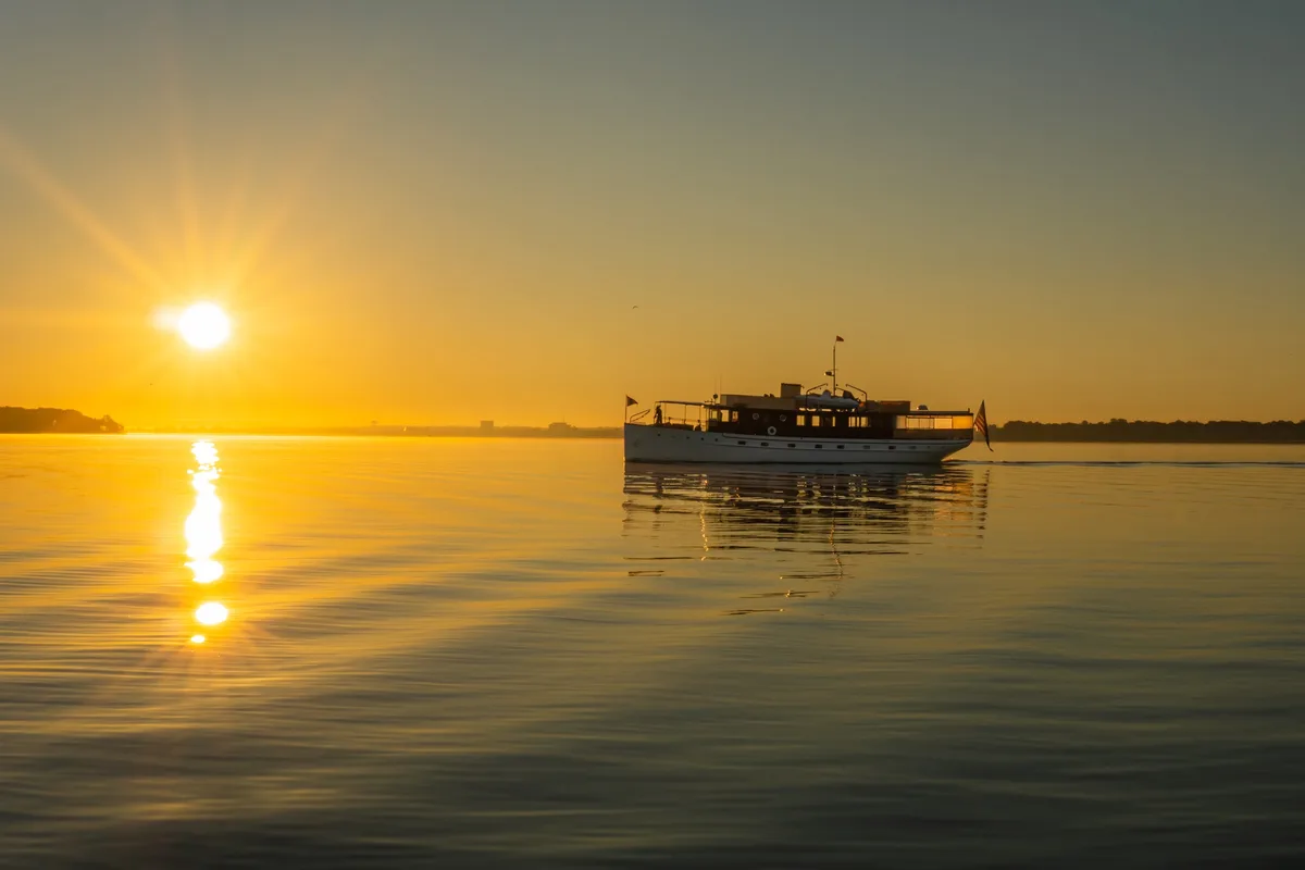 A serene sunset over calm water with a boat silhouetted against the golden sky, its reflection shimmering on the surface…
