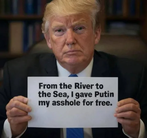A man with blond hair wearing a dark suit and blue tie holds a white sign with black text. The text reads 'From the River to…