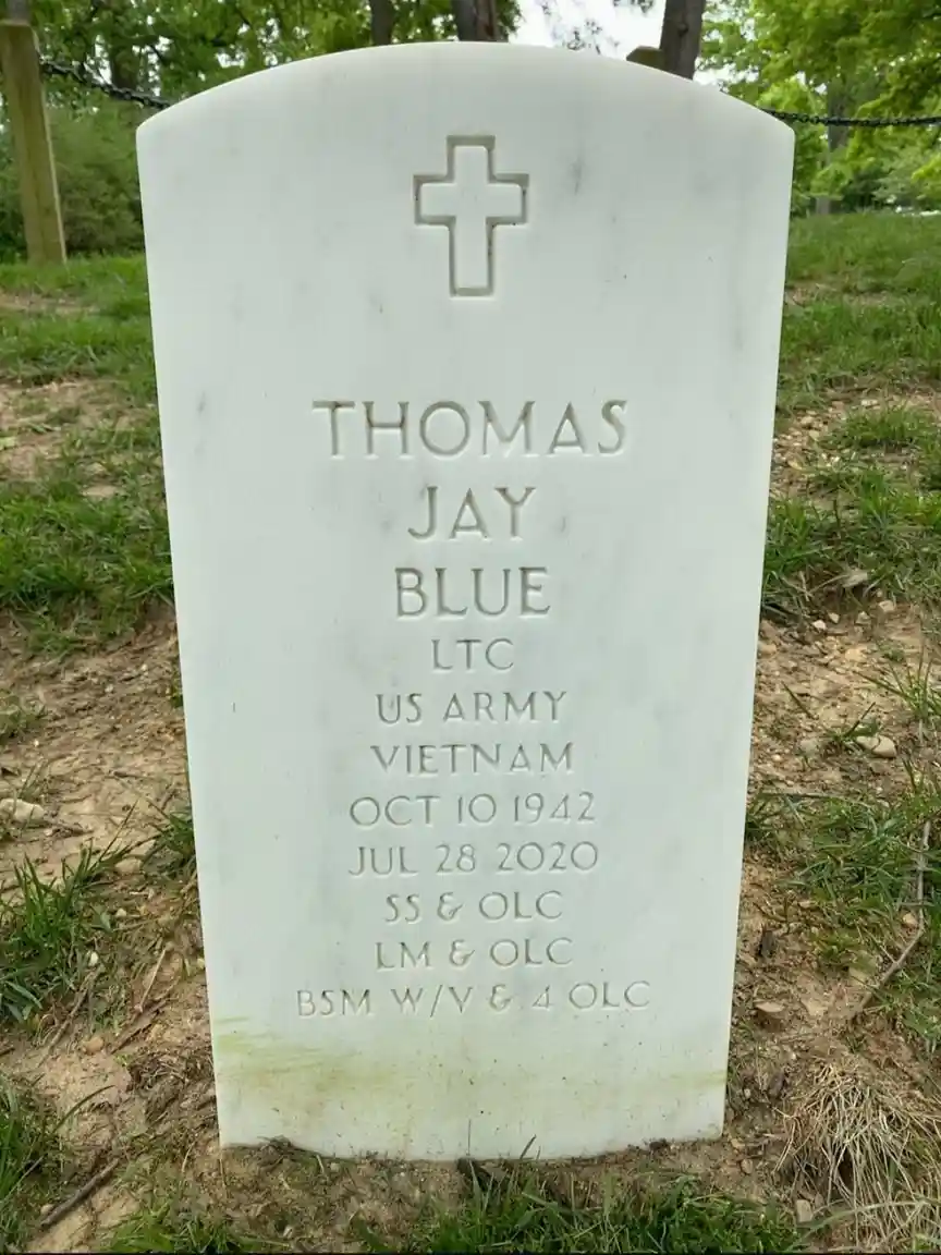 A white marble military gravestone for Thomas Jay Blue, a U.S. Army LTC who served in Vietnam, shows his birth and death…