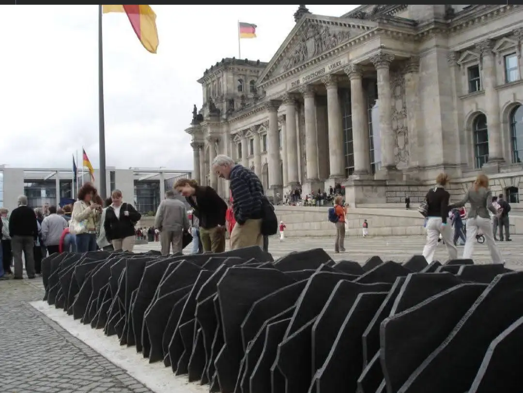 A photo of tourists at the Berlin Reichstag building, with the Holocaust Memorial's black granite slabs in the foreground…