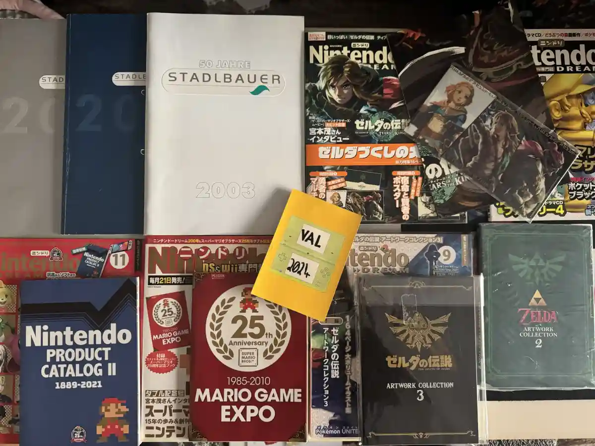 A collection of Nintendo memorabilia including magazines, art books, and catalogs from various years, with a small yellow…
