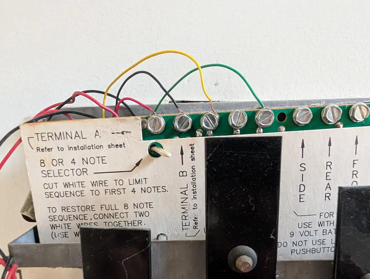 A close-up of an electronic device's terminal board with wires connected to screws, featuring a handwritten label explaining…