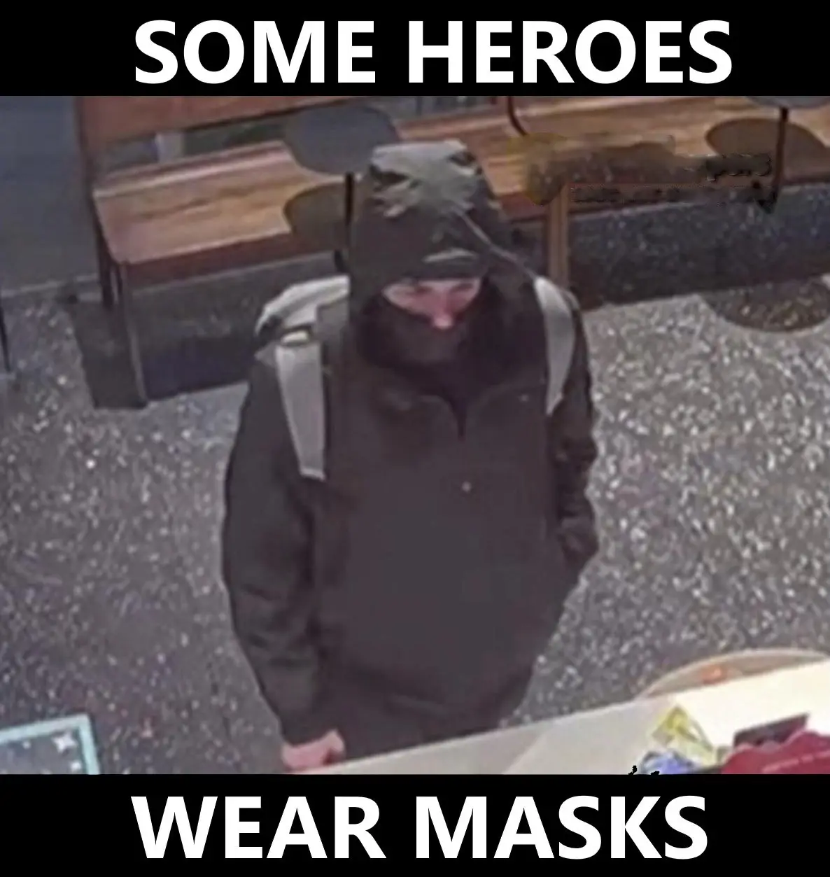 A grainy security camera image shows a person wearing a dark hooded jacket and a black face mask, standing in what appears…