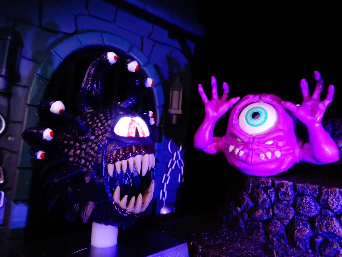 Two monster figures are shown in a dark, stone-walled setting under purple and blue lighting. On the left is a black…