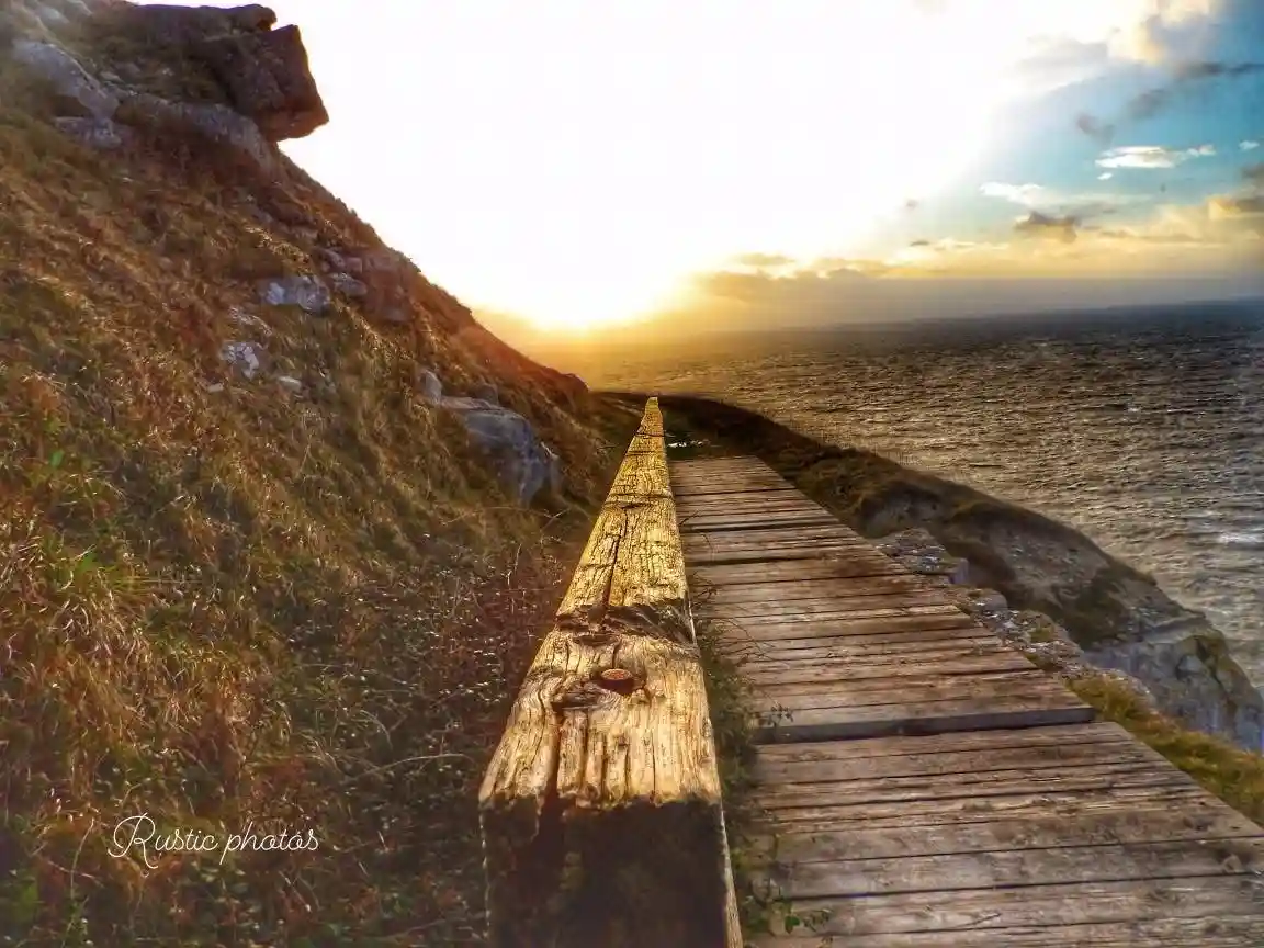 A wooden boardwalk extends along a grassy cliffside toward a sunset over the ocean, with the overlaid text reading 'i'm not…