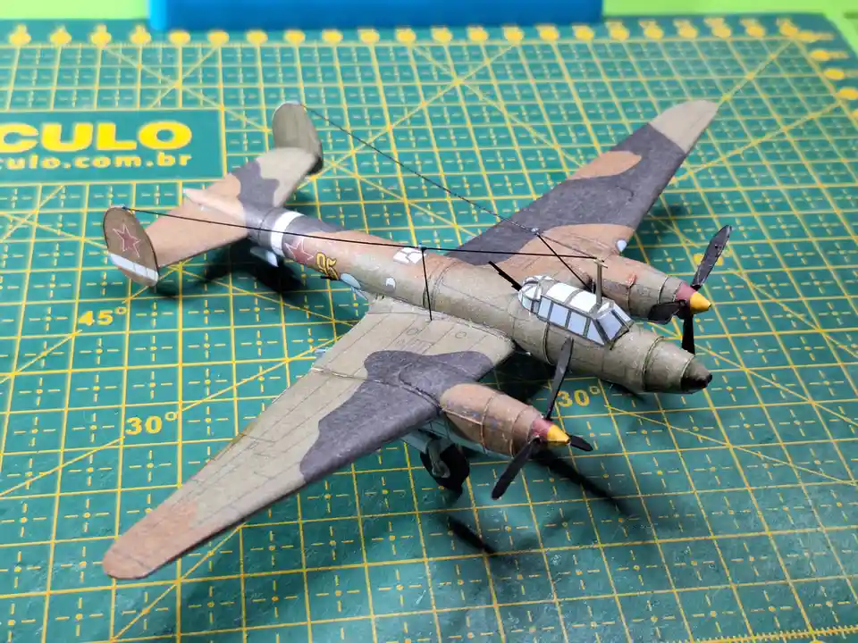 A detailed model of a twin-engine military aircraft with camouflage paint and red star insignia rests on a green cutting mat…