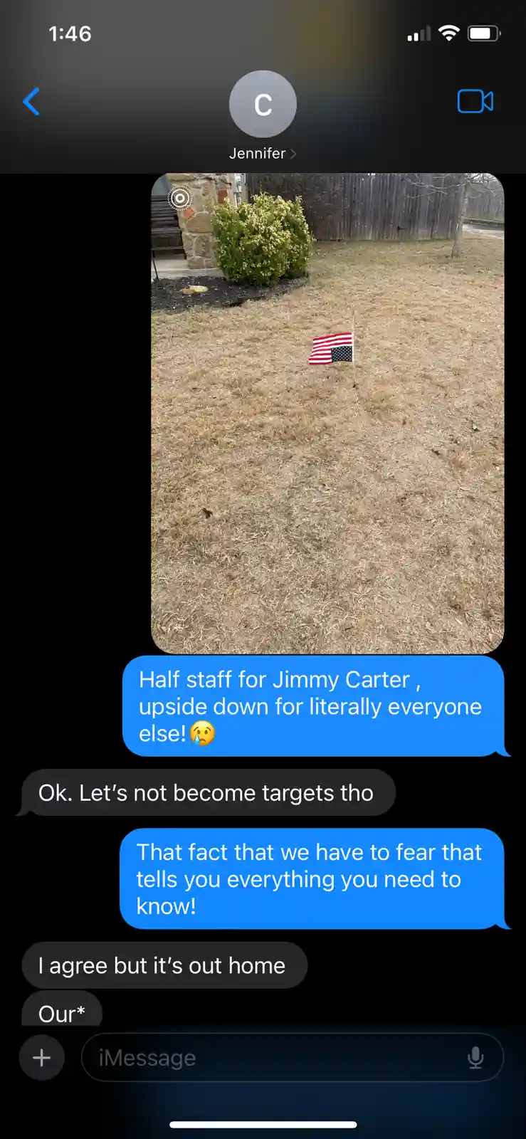 A screenshot of an iMessage conversation shows a photo of a small American flag planted in dry grass, appearing upside down…
