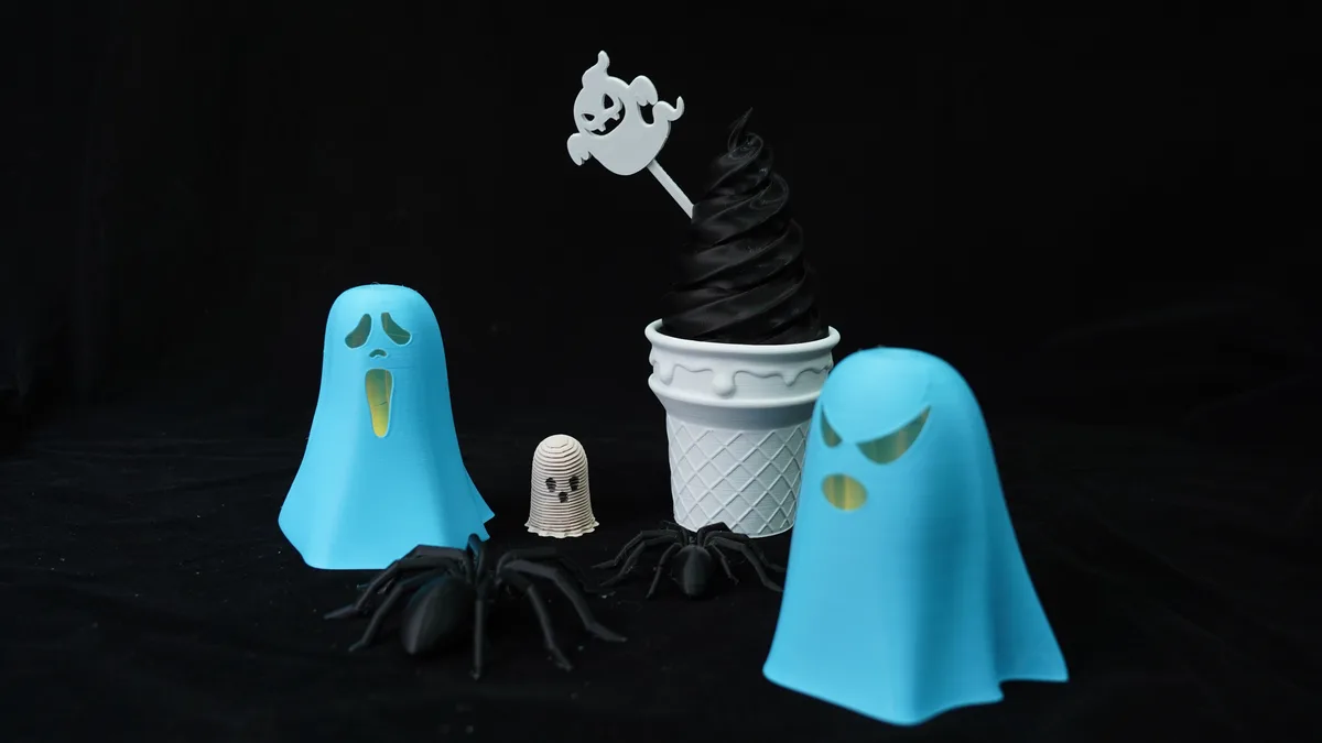 A black velvet background displays Halloween-themed items: two blue ghost figurines, a small white ghost-shaped cupcake…