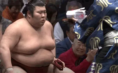 A sumo wrestler, Atamifuji, is shown in a sequence of frames with a shocked or surprised facial expression as a scoreboard…