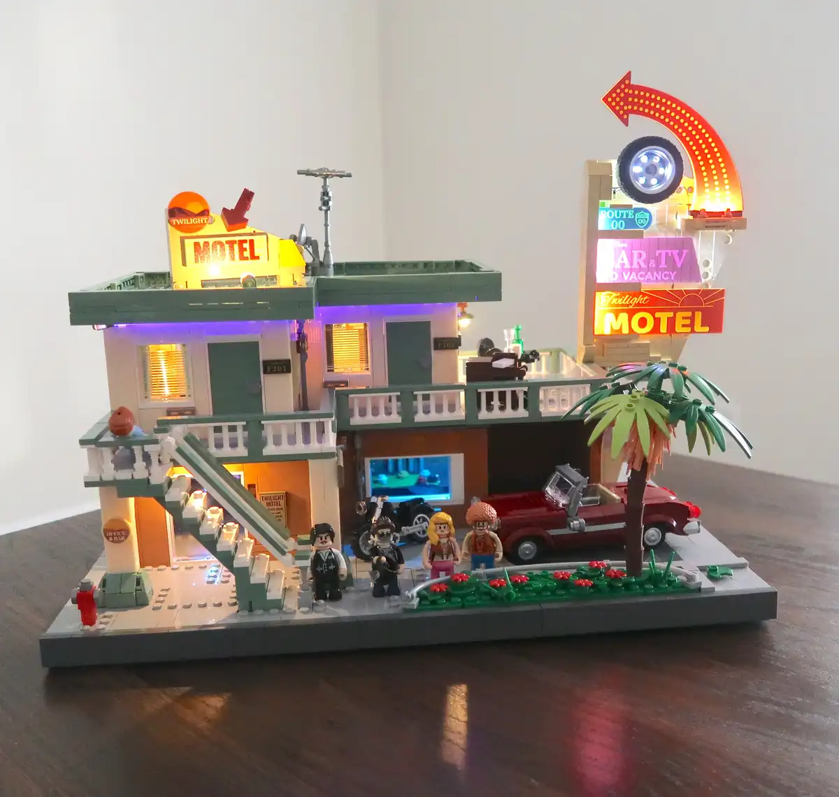 A detailed LEGO model of a retro-style motel with illuminated signs, including a large curved arrow sign with a tire and…