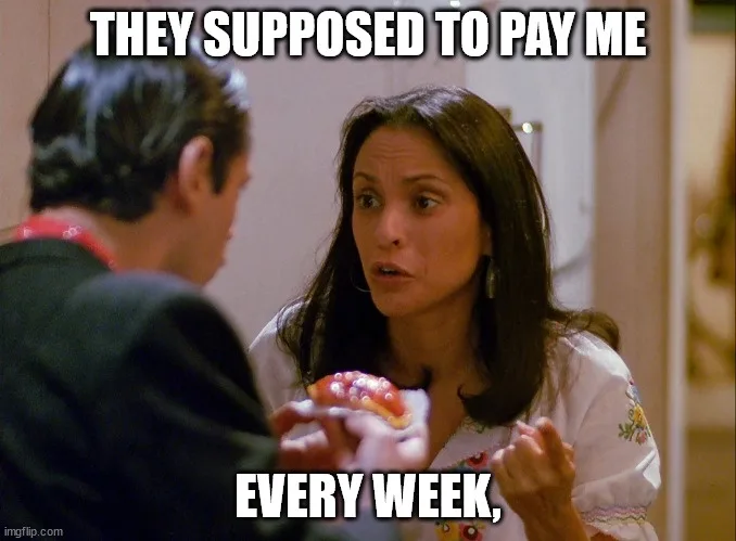A woman with long dark hair and a white embroidered shirt looks surprised and slightly annoyed while holding a small donut…