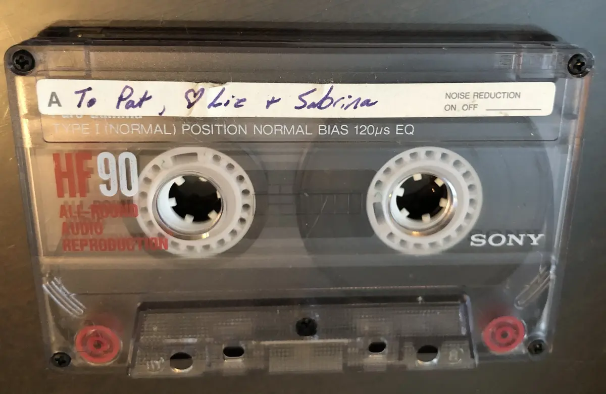 A close-up of a transparent Sony HF90 cassette tape with a handwritten label that reads 'To Pat, ❤ Liz + Sabrina'. The…