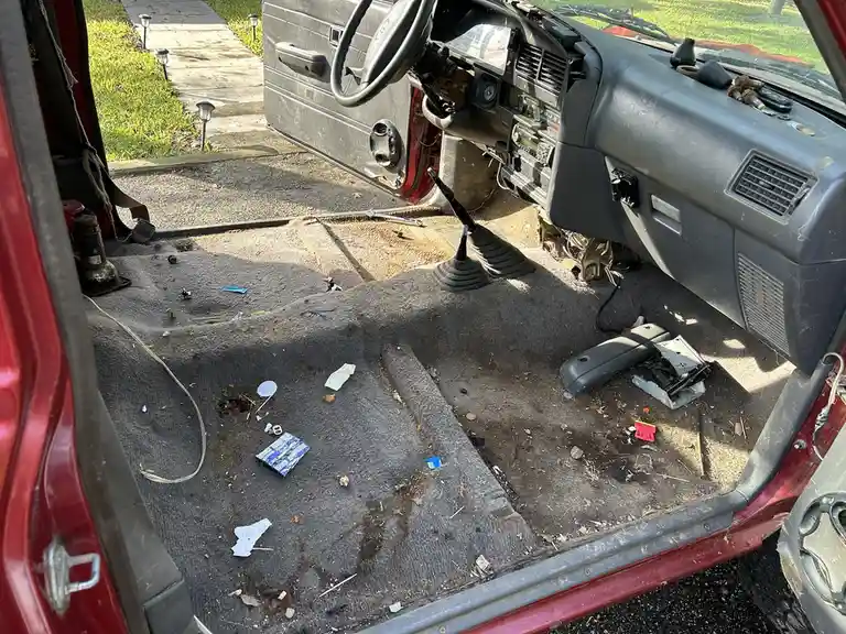 The interior of a red car is shown with its dashboard and steering wheel partially dismantled, revealing exposed wiring and…