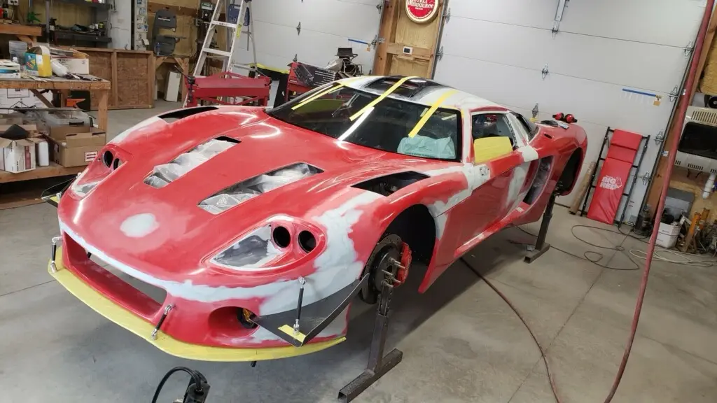 a red sports car is partially painted white in a garage, with yellow tape marking sections, and the text 'this is a car that…
