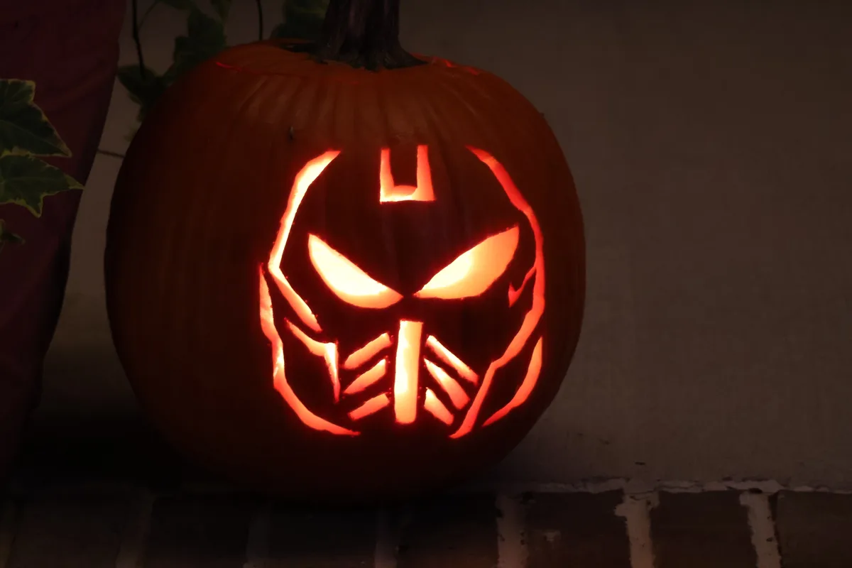 A carved Halloween pumpkin with glowing orange light inside, featuring a face design resembling the Decepticon leader…