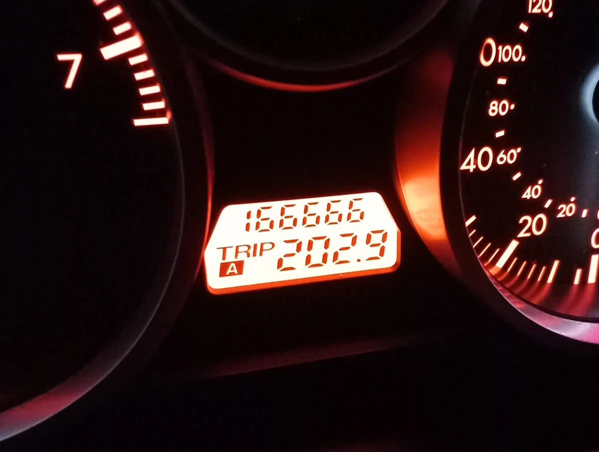 A close-up of a car's illuminated dashboard shows a digital odometer displaying '166666' and a trip meter reading '202.9'…