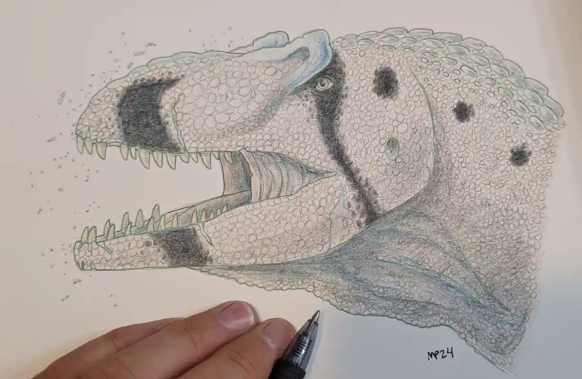 A hand holding a pen is positioned near a detailed colored pencil drawing of a dinosaur's head, which has realistic…