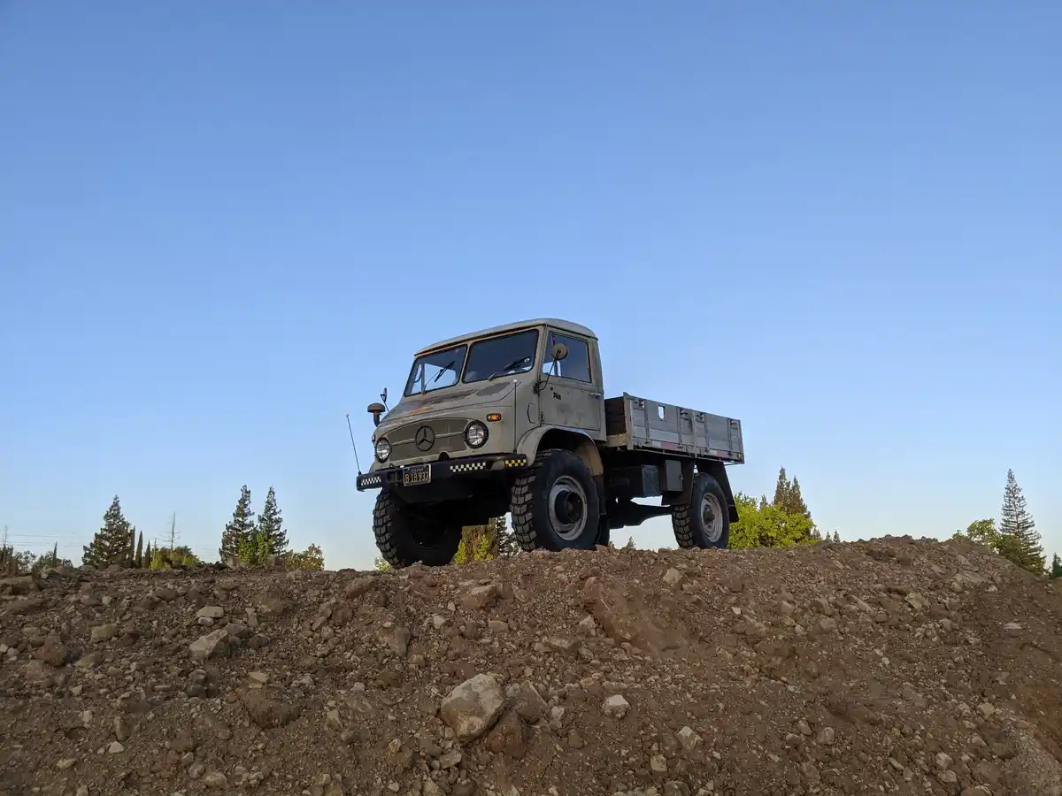 A rugged, olive-green Mercedes-Benz military-style truck with a California license plate (B18933) is parked atop a large…