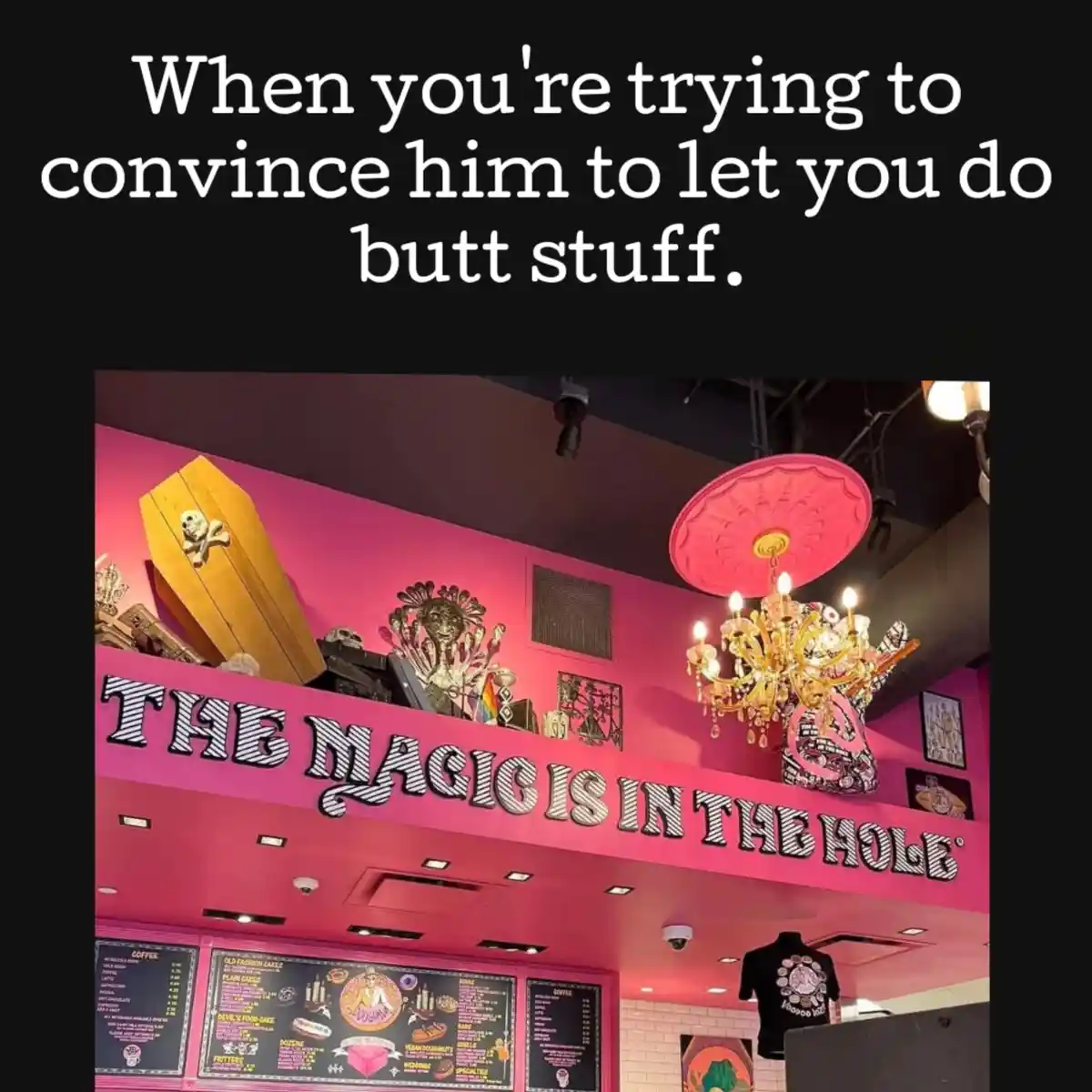 An image of a pink-themed cafe interior with a large sign reading 'THE MAGIC IS IN THE HOLE'. The decor includes a coffin, a…
