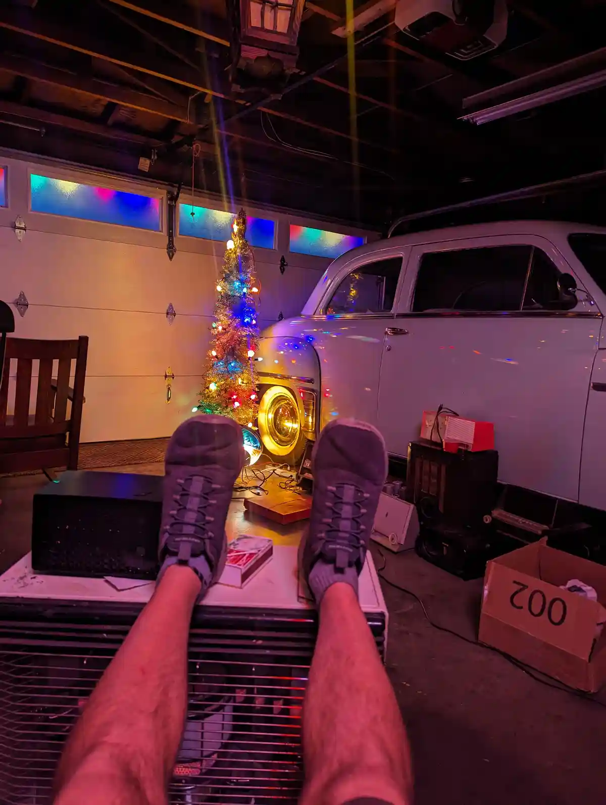 A first-person view shows a person's feet in gray sneakers resting on a white appliance, likely a refrigerator, in a garage…