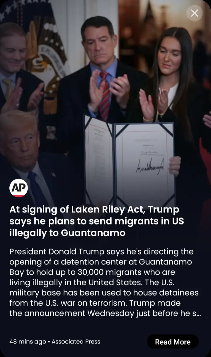 A screenshot of a news article overlaying a photo of Donald Trump seated while others stand behind him clapping. The article…