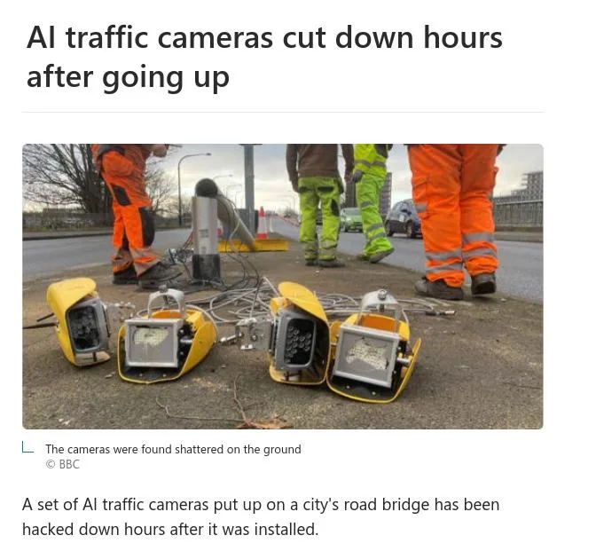 Several shattered yellow traffic cameras lie broken on the pavement, surrounded by workers in orange and green…