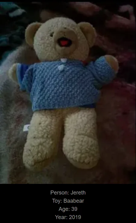 A beige stuffed teddy bear wearing a blue knitted sweater lies on a textured surface. Text overlaid at the bottom identifies…