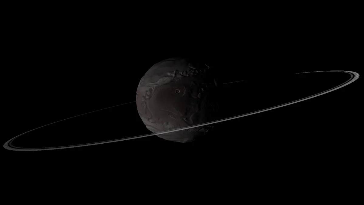 A dark, cratered spherical celestial body resembling a moon is shown against a black background, with a thin, faint ring…