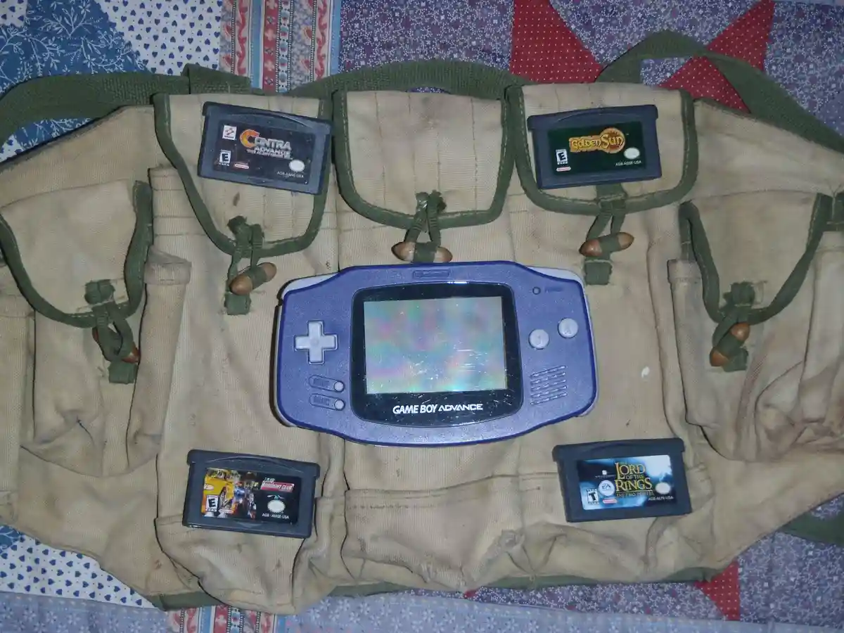 A blue Game Boy Advance sits centered on a tan military-style utility vest with multiple pockets, each holding a game…