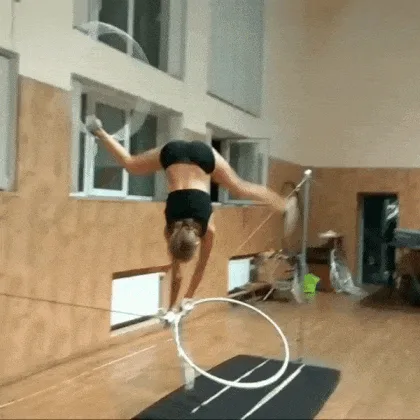 A grid of six images shows a woman in a black sports outfit performing a handstand on a ring apparatus in a gym. She is…