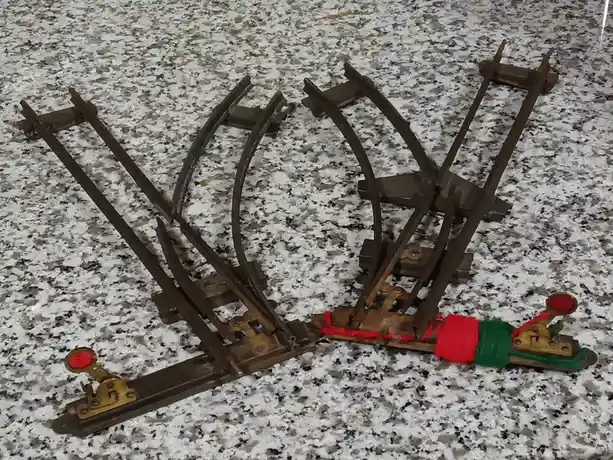 A rusty, broken model train track piece lies on a speckled granite countertop, with a small train engine at its end wrapped…