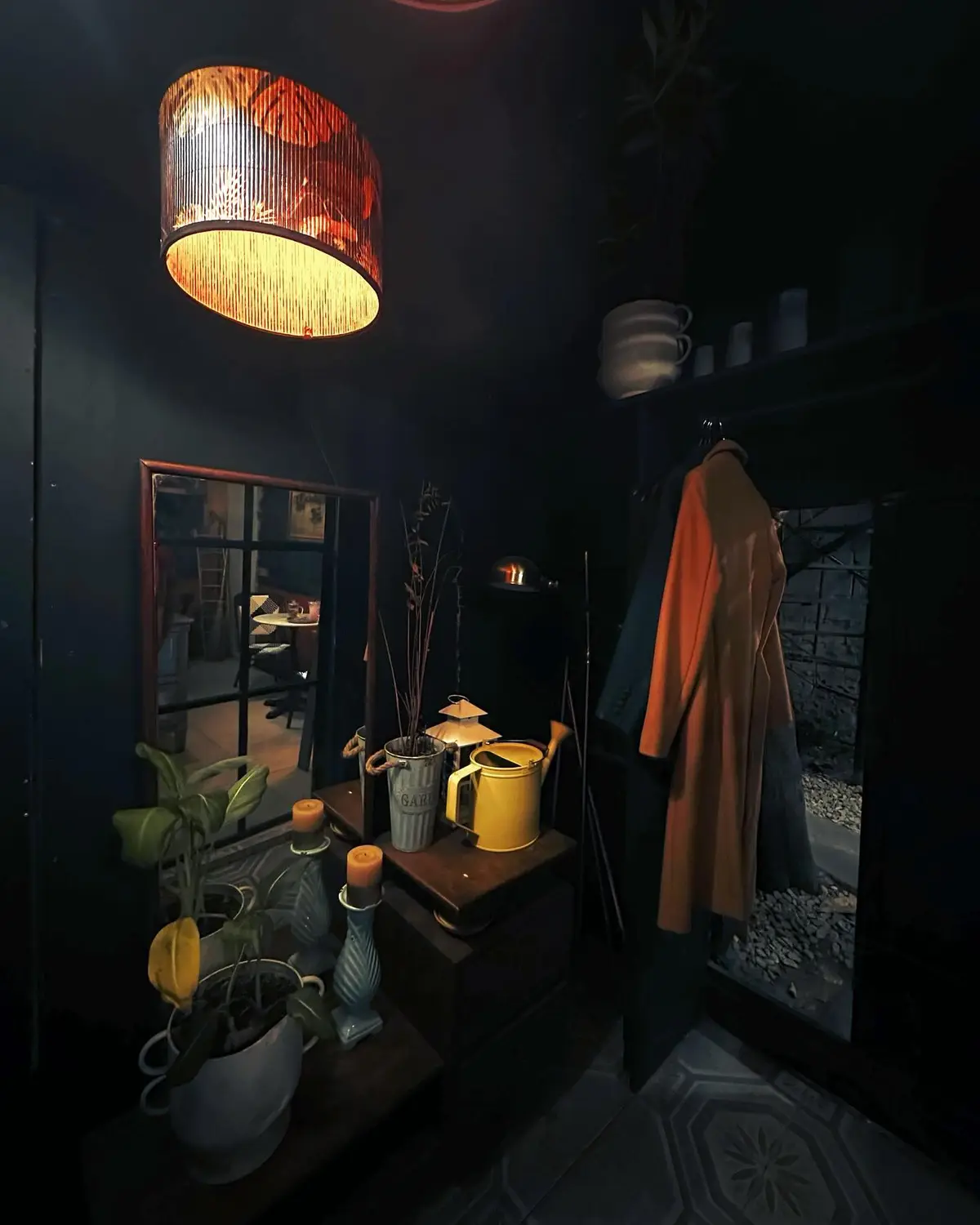 A dimly lit, moody interior space with dark walls, a glowing cylindrical pendant lamp, and a coat hanging on a hook. On a…