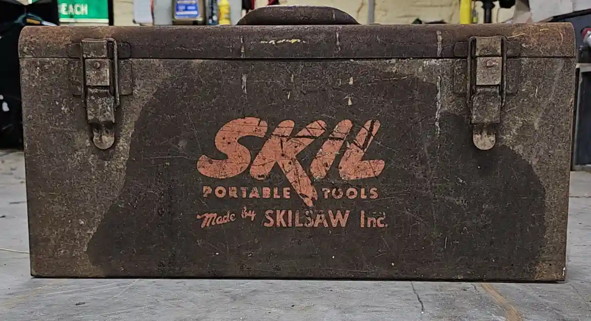 A heavily worn, rusty metal toolbox with faded orange lettering that reads 'SKIL PORTABLE TOOLS Made by SKILSAW Inc.' The…