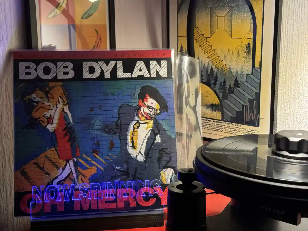 A vinyl record player with a Bob Dylan album titled 'Oh Mercy' standing upright next to it. The album cover features a…