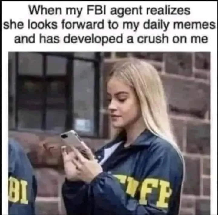A young woman with blonde hair wearing a dark blue jacket with yellow 'FBI' lettering on the sleeve is looking down at a…