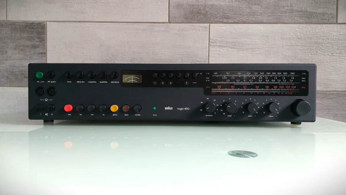 A black Braun regie 450 vintage radio receiver with numerous knobs, buttons, and a frequency display sits on a reflective…