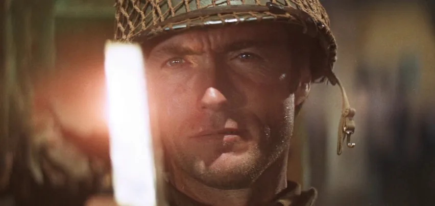 A close-up of a man in a military helmet with a serious, intense expression, holding a glowing white object in front of his…