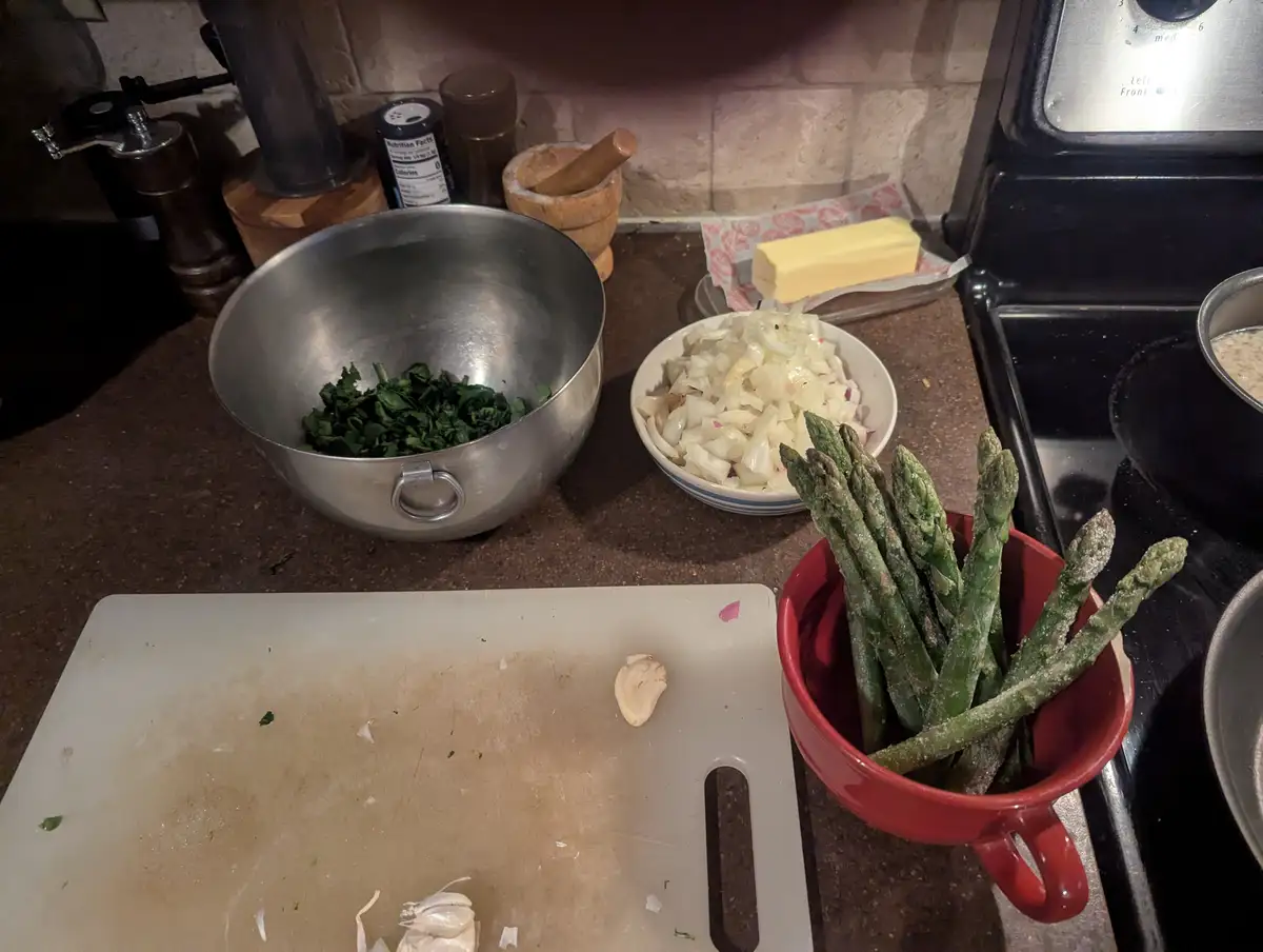 A kitchen counter with cooking ingredients including chopped spinach in a metal bowl, diced onions in a white bowl, and…