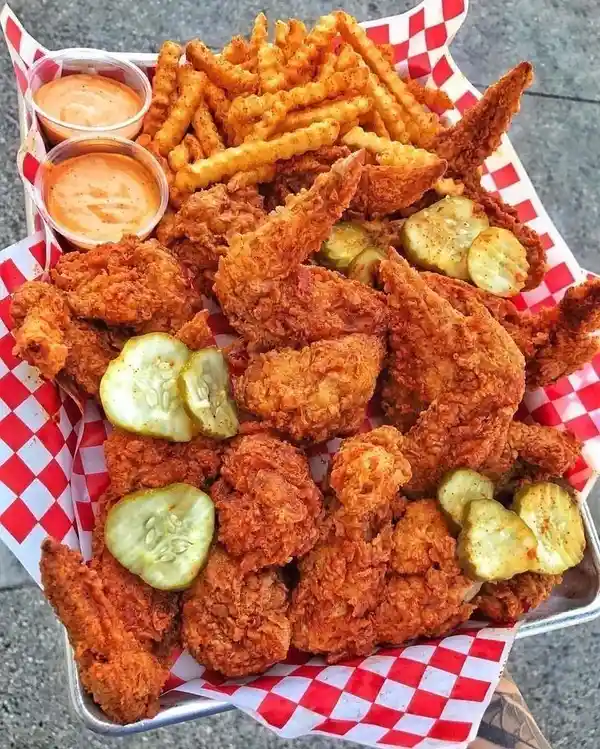 A metal tray lined with red-and-white checkered paper holds a large serving of crispy fried chicken wings, crinkle-cut…
