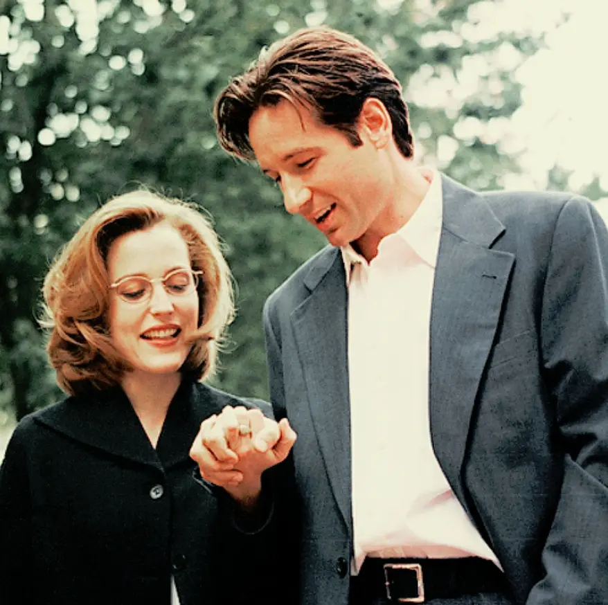 A man in a grey suit and white shirt looks down at a woman's hand holding a ring, while she smiles. The overlaid text reads…