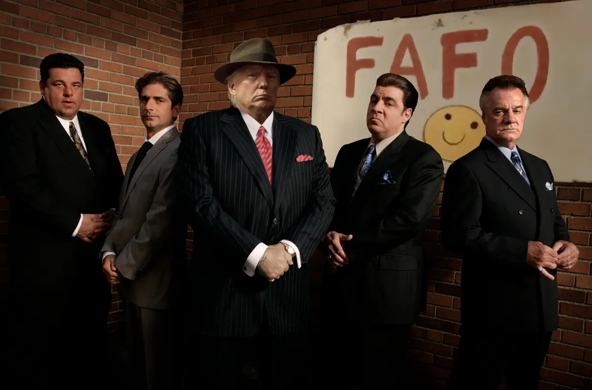 Five men in suits stand in a row against a brick wall, with a faded sign behind them that reads 'FAFO' above a simple yellow…